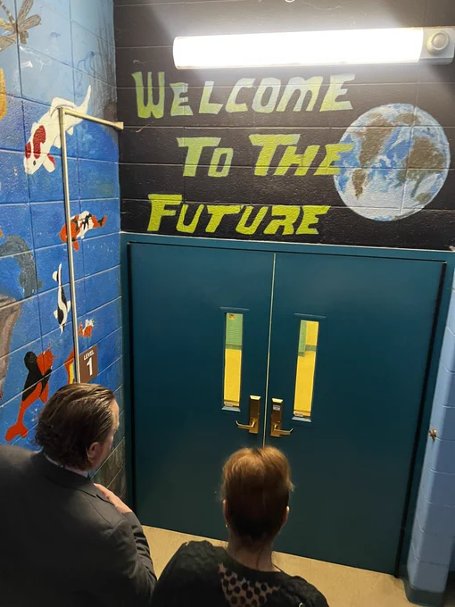Commissioner Infante-Green and Director Ken Hopkins walk down the stairs. A mural is painted featuring the words “welcome to the future.”