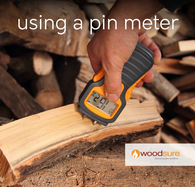 A piece of cut firewood on a stump with a human hand holding a pin meter to check the moisture content, the meter reading is 16.2%. The words, 'using a pin meter', are across the top centred in large font. The 'Woodsure assured quality woodfuel' logo is towards the bottom right-hand corner.
