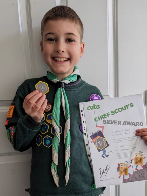 A Cub Scout holding a silver award badge and a certificate