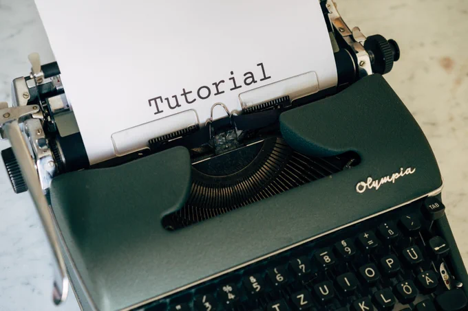 Eine schwarze Schreibmaschine mit einem eingespannten weißen Blatt Papier auf dem das Wort "Tutorial" zu lesen ist.