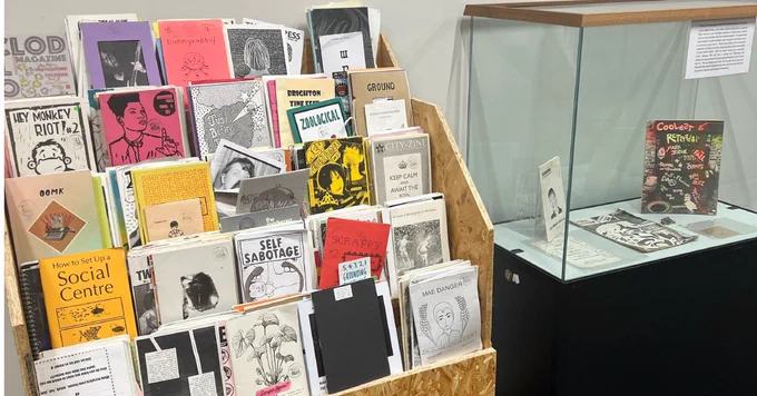 Image of the zine maker space. Complete with a zine library, instructions on how to make a zine, a zine donation box, a zine vending machine and a printer