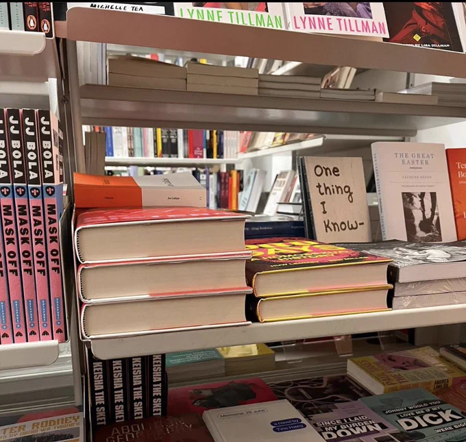 A shelf of stacked books at eye height where only the white pages can be seen, on top is the orange and white spine of the book