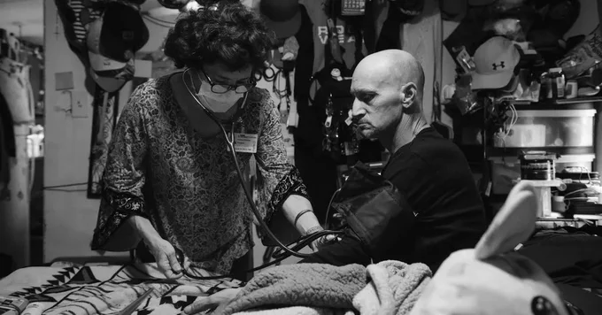 Black and white image of Dr. Elizabeth De Pirro treating Richard Walker at his home in Albuquerque. Credit...Kholood Eid for The New York Times