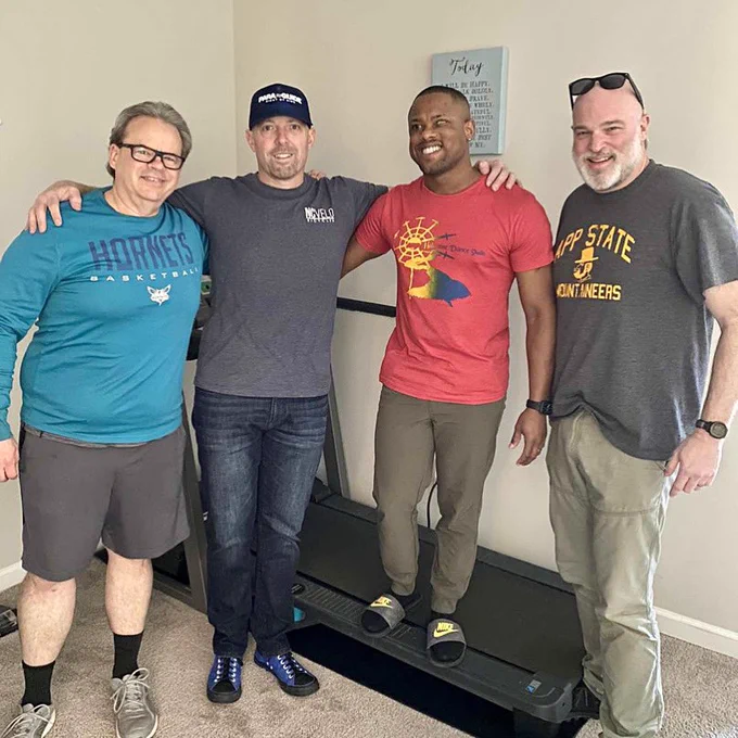 Four men are gathered and smiling with the treadmill inside DJs house