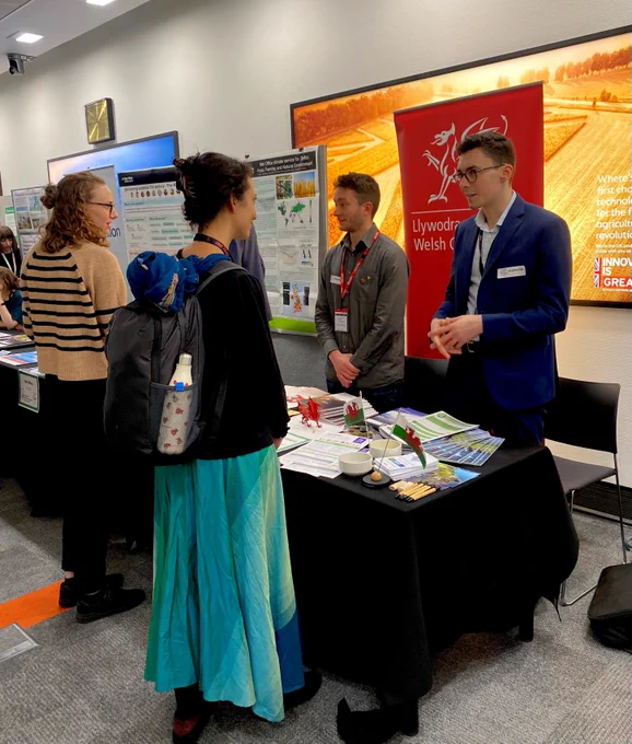 Image of Welsh Government stand at the Circular Economy event. Two staff members from Welsh Government stood behind the table talking to attendees of the event