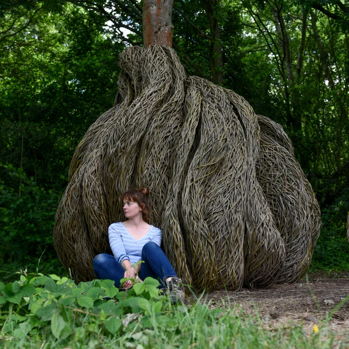 Laura Ellen Bacon sitting on the floor in front of her tree sculptures