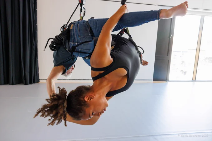 Two female aerial dance performers hang upside down from a harness