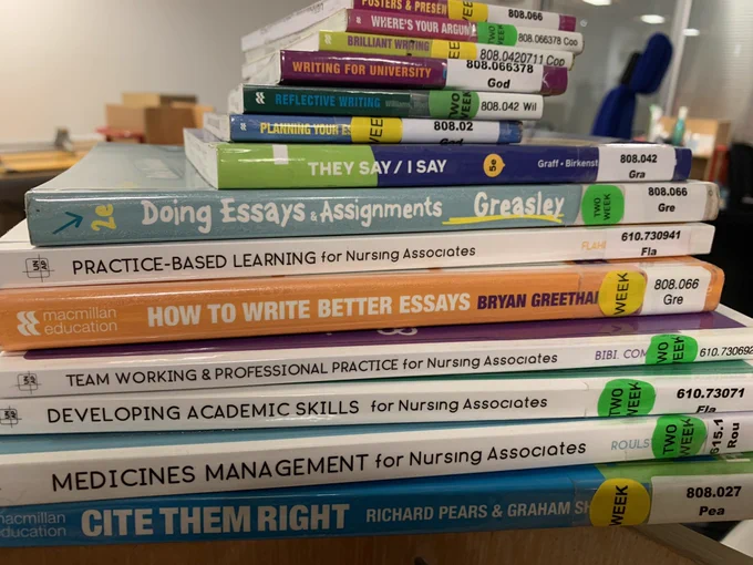 A photo of a pile of books with just their spines visible. They are a mix of Trainee Nursing Associate & academic study skills books.