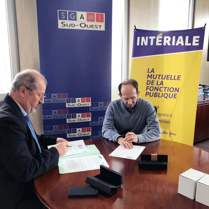Deux personnes signent des documents sur une table ronde devant les kakémonos de la SGAMI Sud-ouest et d'Intériale. 
