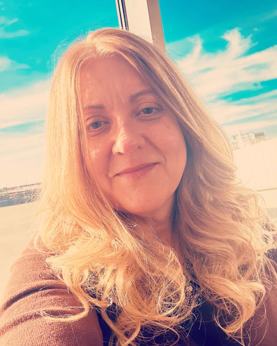 Anne in front of the window at the airport in Louisville with a beautiful blue sky in the background