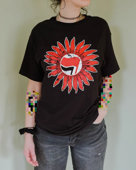 photo of a person wearing a black shirt with a red sunflower in the center. inside the flower, there's a black and red flag. artist: nightowl custom apparel.