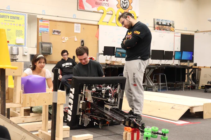 Three students changing the battery of a robot.