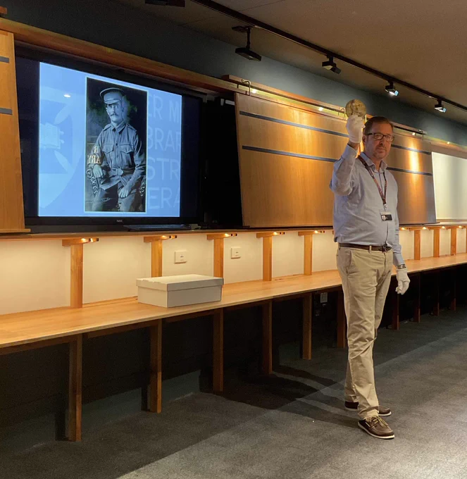 Fryer Librarian, Simon Farley, holding the WWI memorial medal of Charles Fryer - a portrait of Charles is on the screen behind him.