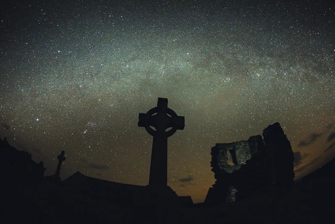 photo by Steve Porter. Dark starry night over Bardsey cemetery. Celtic cross in foreground. 