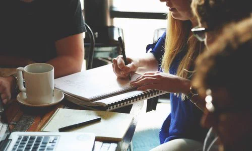 Students in group discussion taking notes on a table with a laptop and cup of coffee beside it