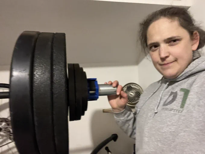 Rachael standing near a barbell@with lots of plates on it wearing a greet disrupt texts hoodie