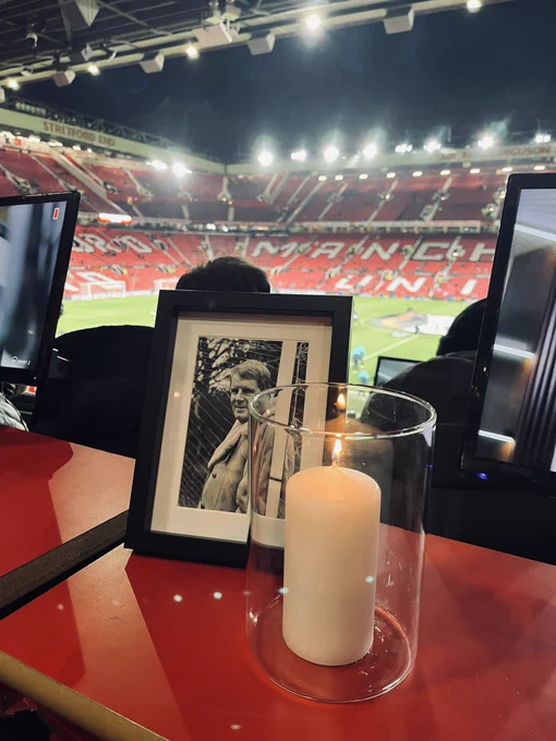 An image of John Motson laid in commentary position at Old Trafford, with a candle lit next his photo.