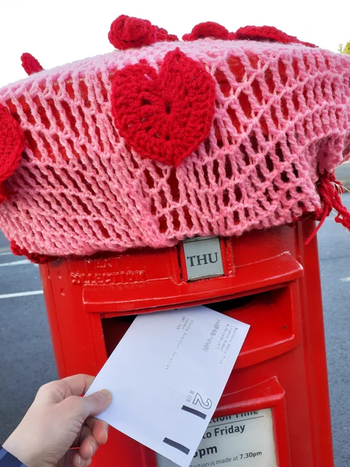 A hand posting a UCU ballot paper in a red postbox topped with a pink crochet decoration