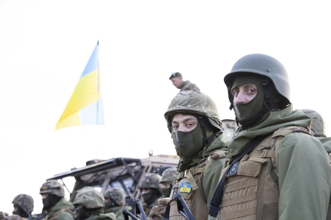 Two Ukrainian recruits look onwards as the Ukrainian flag flies atop an armoured vehicle