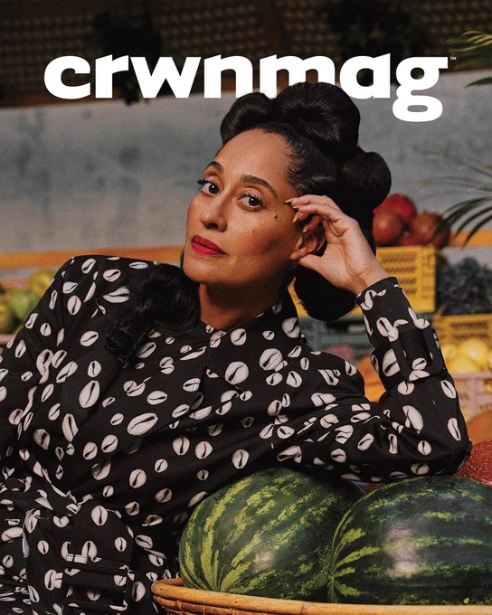 Portrait of Tracee Ellis Ross on the cover of CRWNMAG. She is wearing a fabulous cowrie she’ll patterned jumpsuit with a matching trench coat. She is pictured in front of a North African style bazaar fruit stand.