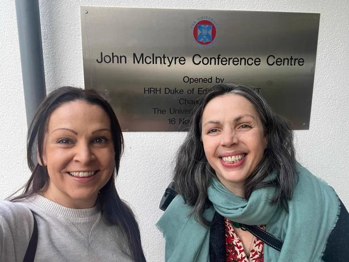 Colour photo of two lobular breast cancer patient advocates and Lobular Breast Cancer UK Trustees standing outside a conference centre. Both have long dark hair and are smiling at the camera.