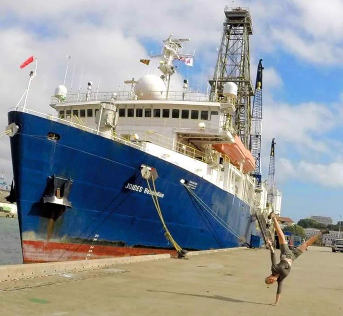 Photo of a vessel and a someone doing a one handed handstand 