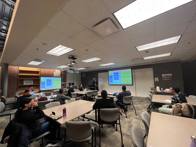 Photo of Cambio Fellow, Andrés Mesa presenting his research to Mizzou alumni and students. Students are facing Andrés with his colorful PowerPoint presentation on display. 