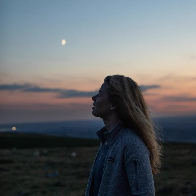 Imogen Napper looking up to the sky at dusk. The moon appears above a cloud.