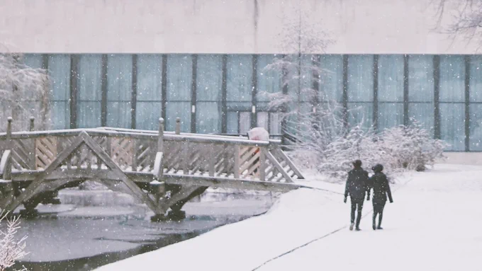 Western Bank Library and park bridge covered in snow, people walking in foreground
