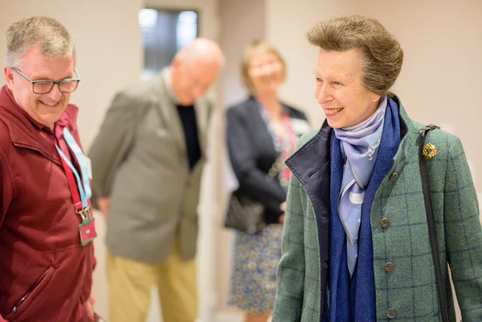 Her Royal Highness The Princess Royal is to the right of the photo and she is talking to a Hearing Dogs for Deaf People volunteer.