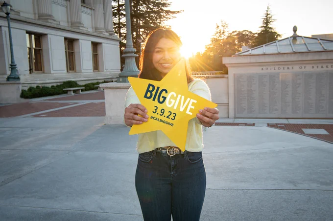 A woman holds a star-shaped sign with the words “Big Give” and the date “3.9.23.”