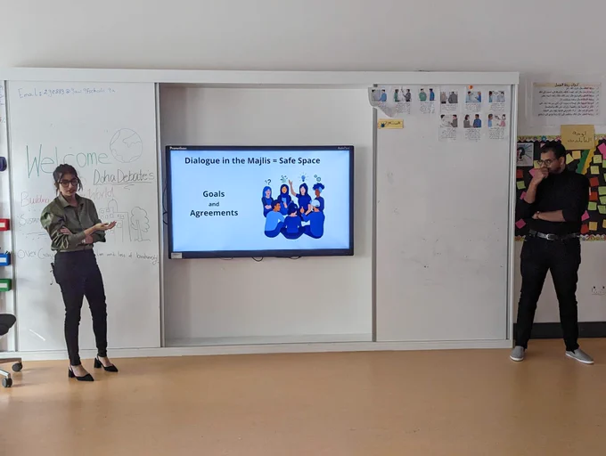 Two young people stand in front of a presentation titled "Dialogue in the Majilis   Safe Space"