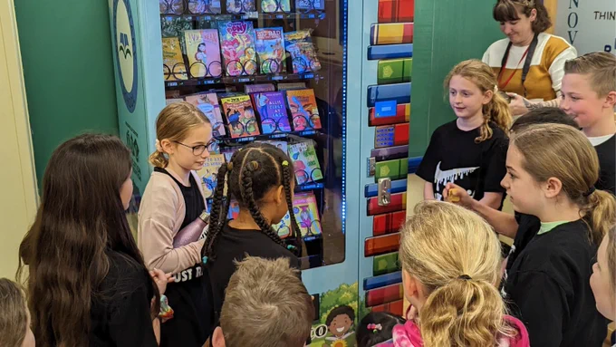 children gathered around a vending machine that dispenses books