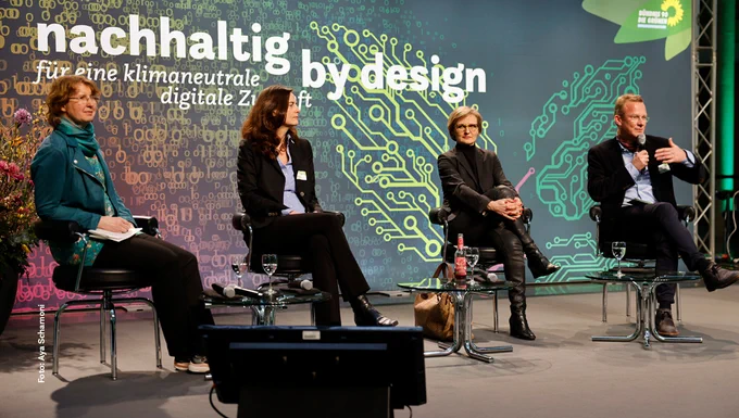 Auf dem Foto ist die Bühne der Konferenz "Nachhaltig by design – für eine klimaneutrale digitale Zukunft" zu sehen. Darauf sitzen, von links nach rechts: Staatssekretärin BMUV Dr. Christiane Rohleder, Alexandra Geese MdEP, Parlamentarische Staatssekretärin BMWK Franziska Brantner und Sprecher für Digitales Maik Außendorf (Moderation).