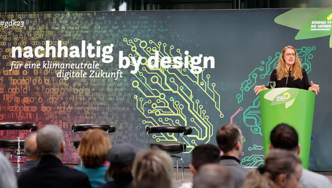 Auf dem Foto ist die Fraktionsvorsitzende Katharina Dröge  auf der Bühne der Konferenz "Nachhaltig by design – für eine klimaneutrale digitale Zukunft" zu sehen. Sie steht am Rednerpult. Im Vordergrund sieht man verschwommen das Publikum.
