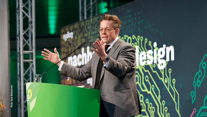 Auf dem Foto ist der stellvertretende Vorsitzende Konstantin von Notz auf der  Bühne der Konferenz "Nachhaltig by design – für eine klimaneutrale digitale Zukunft" zu sehen. Er steht am Rednerpult und hebt die Arme bei seiner Rede.