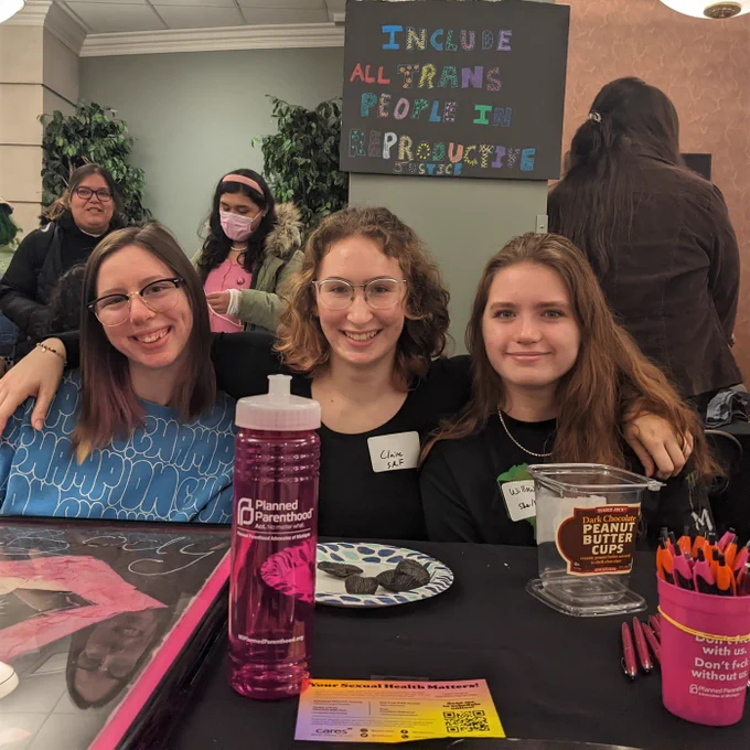 Three students sit together tabling for the CCE Students for Reproductive Freedom program. Table has flyers, pens, and a Planned Parenthood water bottle.