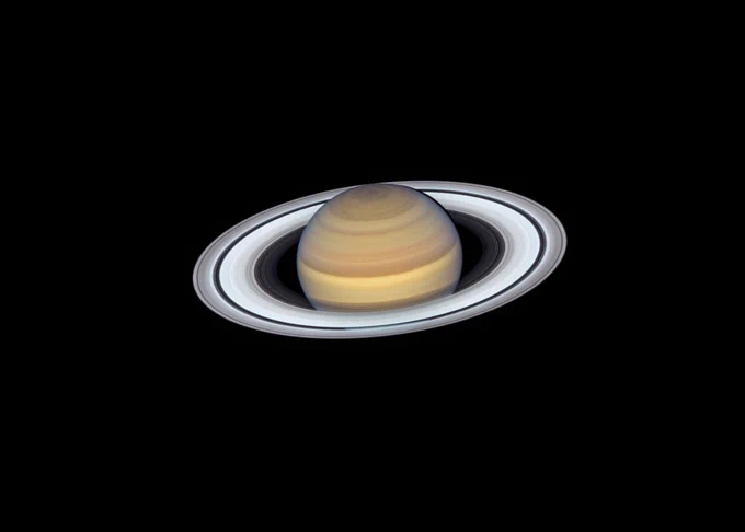 Hubble Space Telescope image of Saturn. The Planet has shades of tan in horizontal rings and the rings around the planet are white. The rings are more visible in the front and on the sides of the planet. 