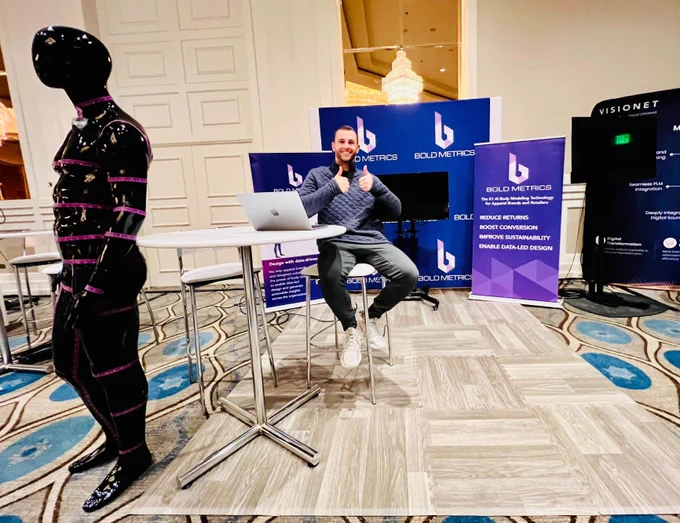 man giving a thumbs up sitting at an event booth with a mannequin in the foreground
