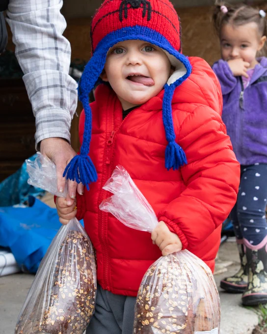 A young child holds a bag of recently delivered local bread and smiles.