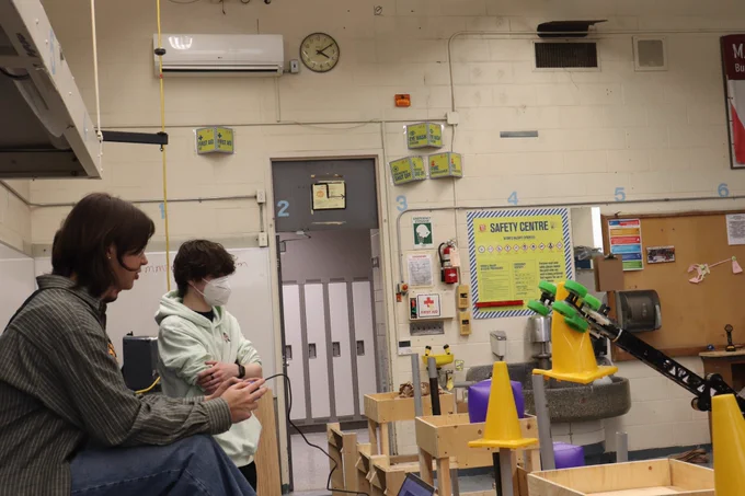 Two students watching robot place cone.