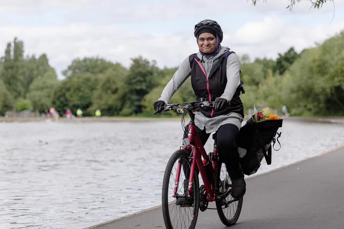 Person cycling beside a pond with flowers in panniers