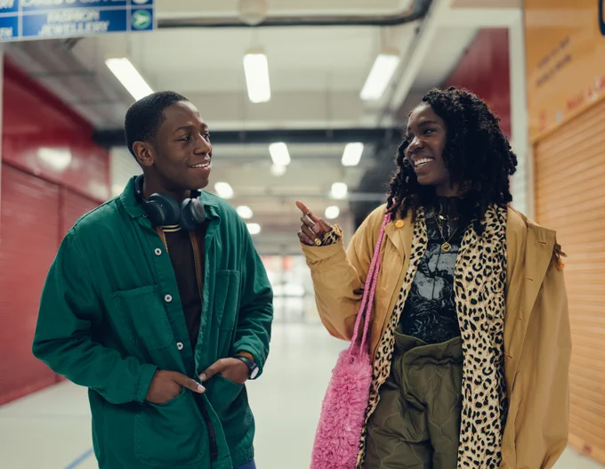 Still from RYE LANE of a woman laughing and pointing at a man who smiles lightly in a bright but closed market.