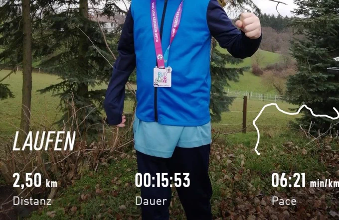 Ein Junge steht vor ein paar Nadelbäumen, vor grüne Weiden.
Der Junge ist blau angezogen- Jacke/  Shirt/ Hose. 
Laufdaten : 2,5km / 15.53min / pace - 6:21min/km