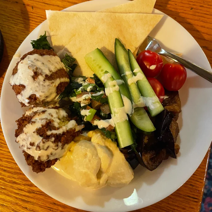 A plate of food from CSI Annex's ritual Get the Scoop, featuring flatbread, vegetables, hummus, falafel, tahini, and tabbouleh.