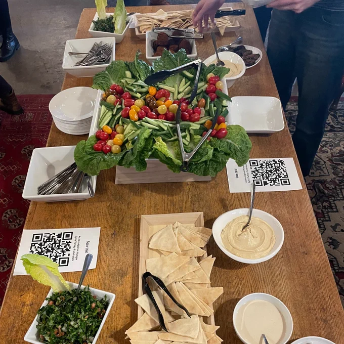 A spread of food for CSI Annex's ritual Get the Scoop, featuring flatbread, hummus, falafel, eggplant, tahini, vegetables, and a simple tabbouleh.