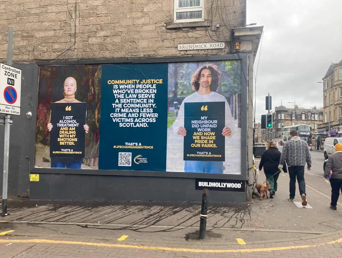 Two large posters with people holding billboards and one with text only on Brunswick Road in Edinburgh