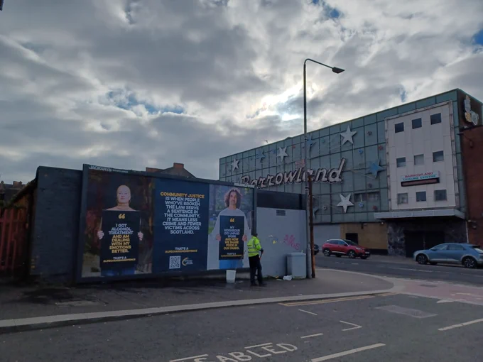 Two large posters with people holding billboards and one with text only outside Barrowland Ballroom in Glasgow