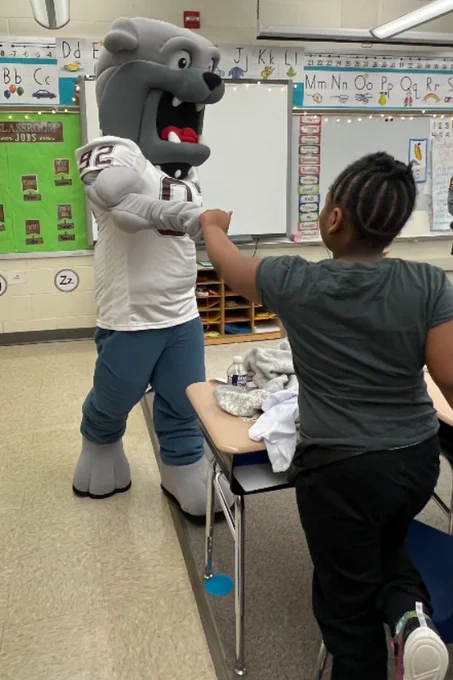 Bulldog mascot fist bumps child in elementary school classroom