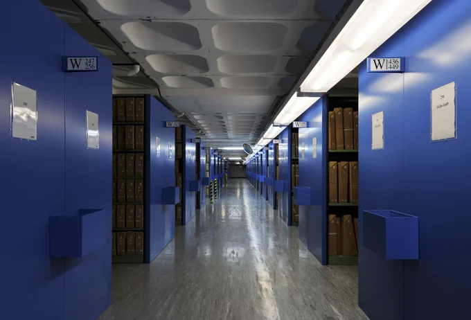 Inside one of The National Archives' repositories. Image features rows of blue shelving containing boxed files.